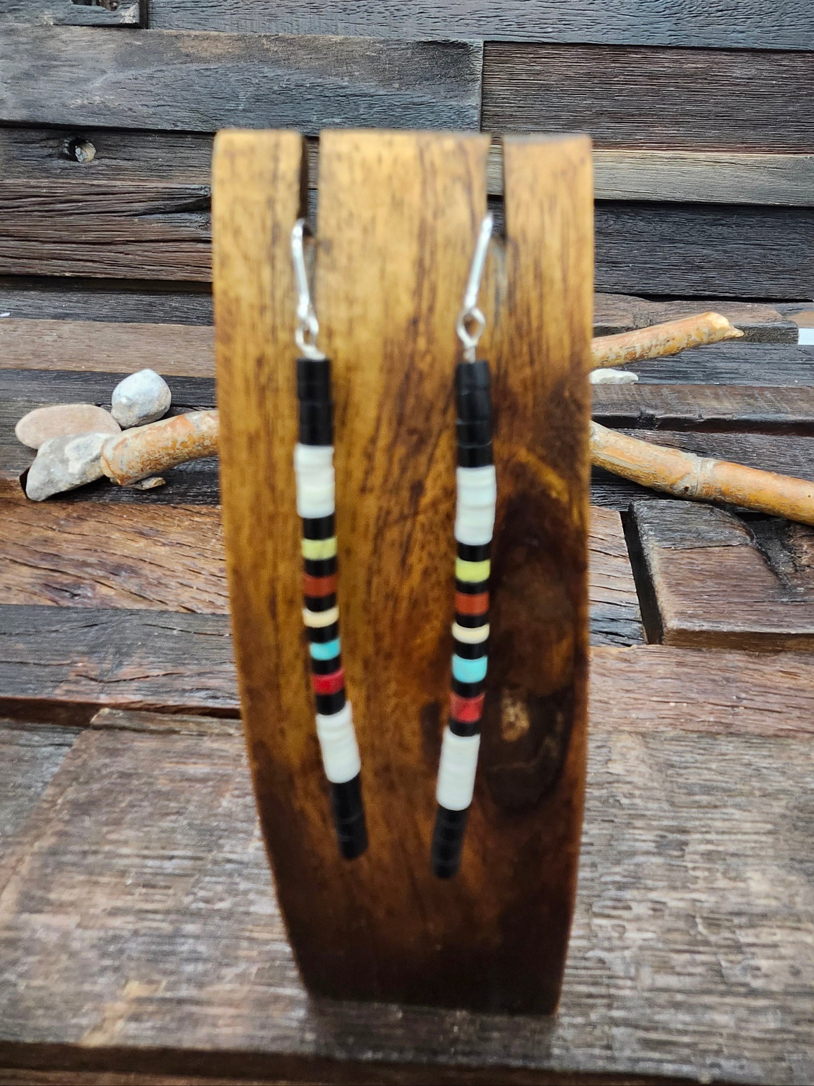 A pair of long beaded dangle earrings displayed on a wooden stand, set against a rustic wooden plank background.