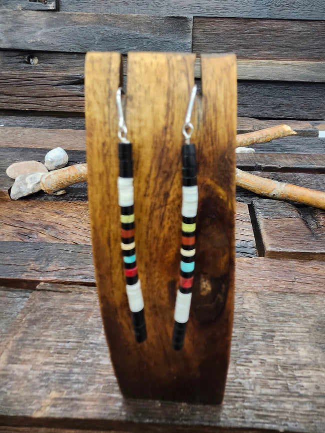 A pair of long beaded dangle earrings displayed on a wooden stand, set against a rustic wooden plank background.